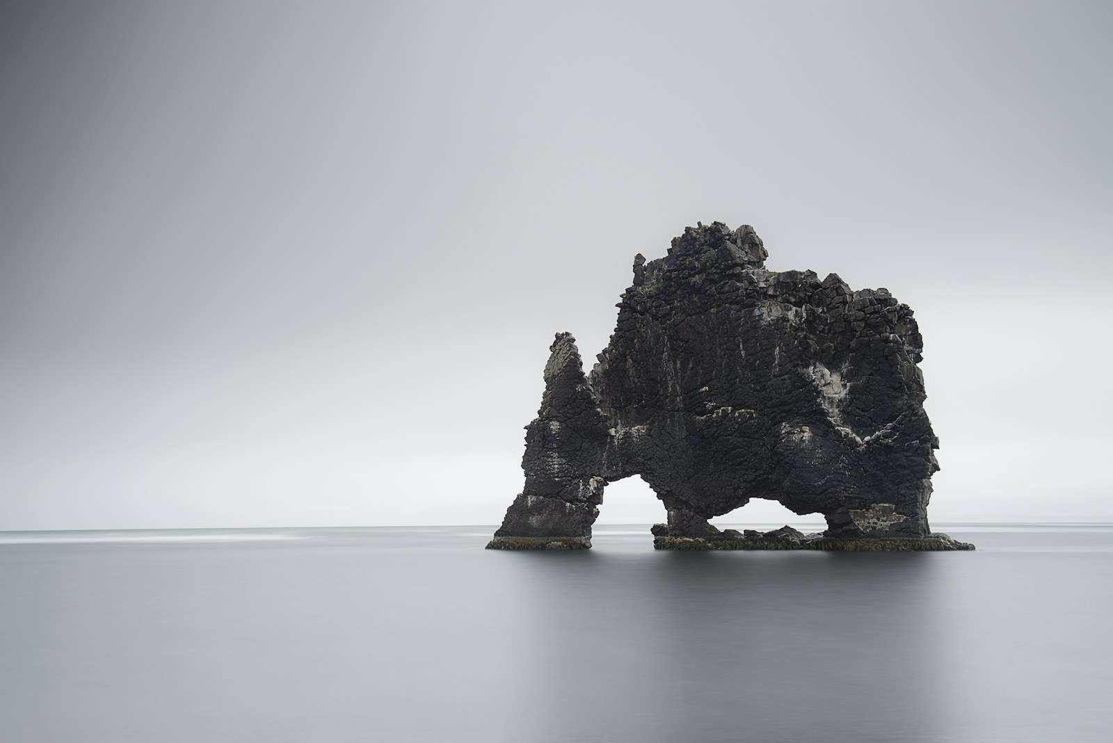The Hvítserkur sea stack standing in still grey water and mist